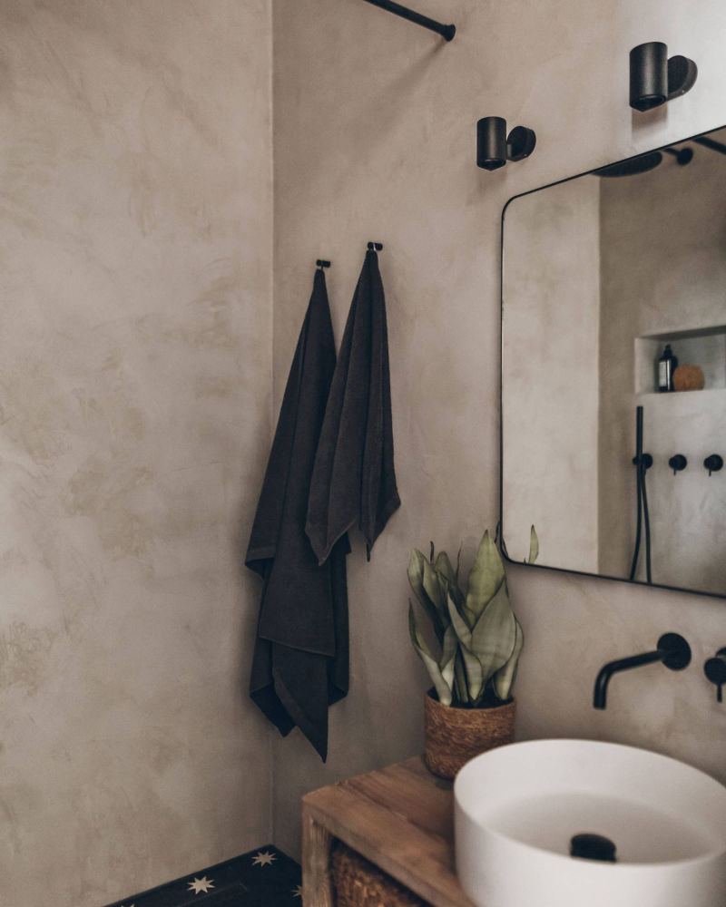 Beige bathroom wall with a black tap and slim-framed mirror
