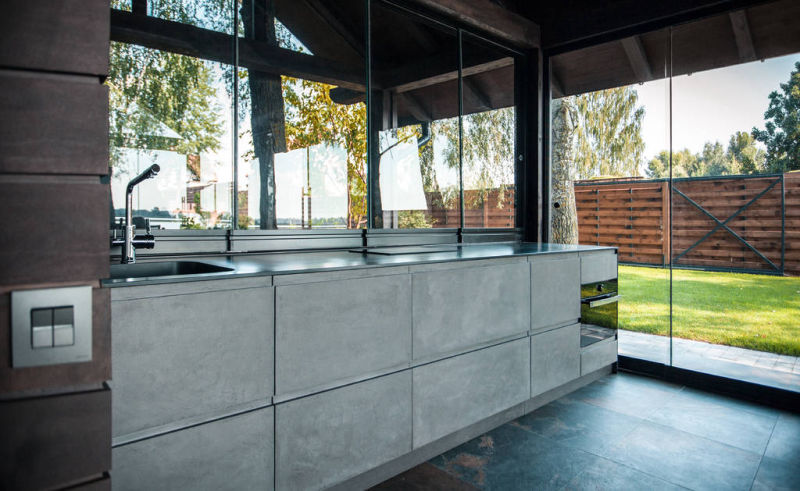 Grey cabinets and floor in a glazed kitchen opening onto a garden