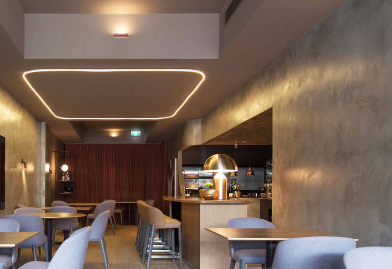Restaurant seating area with grey walls beneath an illuminated ceiling